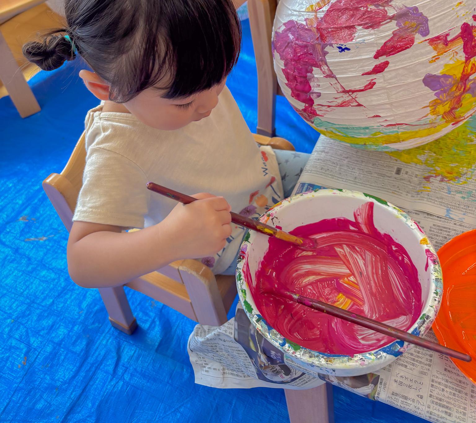 ピンクの絵の具で丁寧に混ぜる子ども