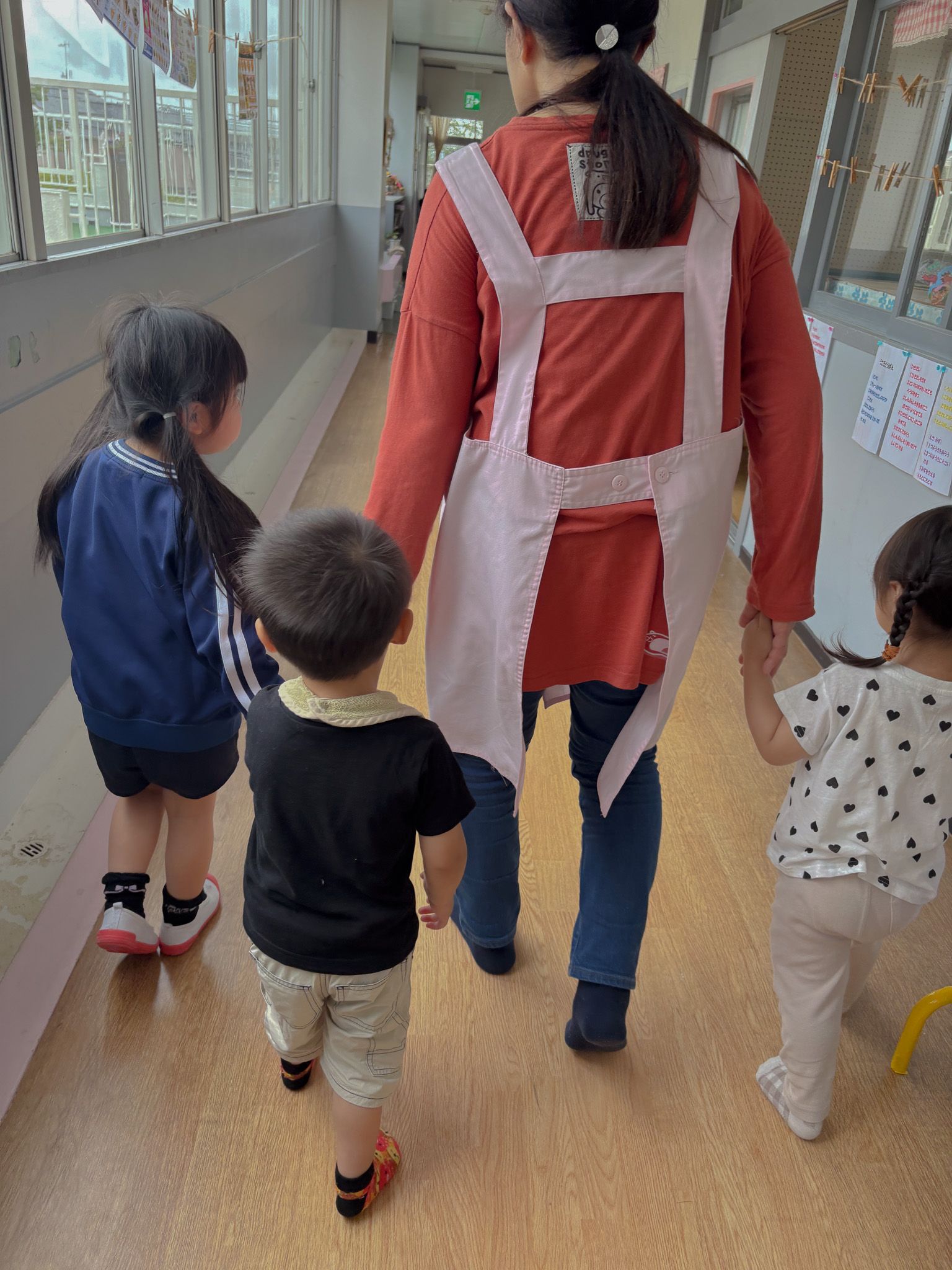 保育園児たちと手をつなぎながら幼稚園をあとにする場面
