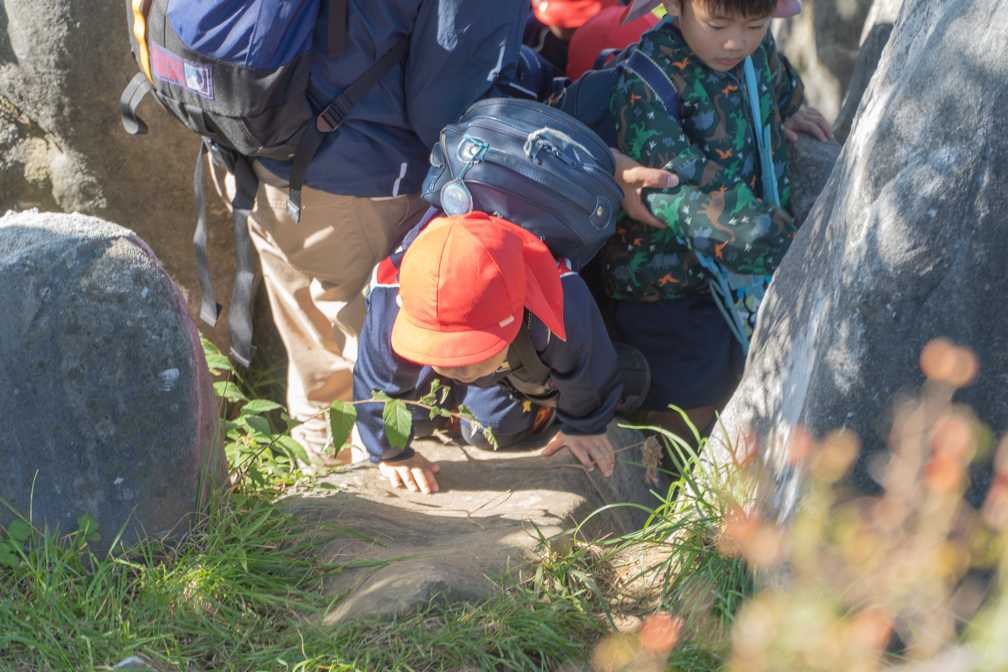 岩をよじ登る子どもと見守る先生